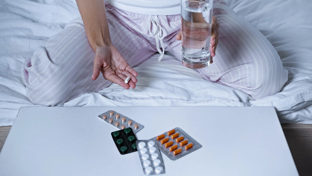 Cropped view of sick woman holding pill and water near table with medications