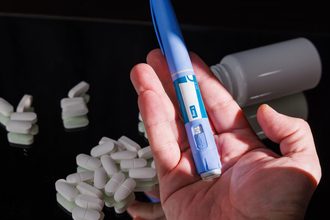 Hand holding a GLP-1 pen with medicine pills on black mirror.