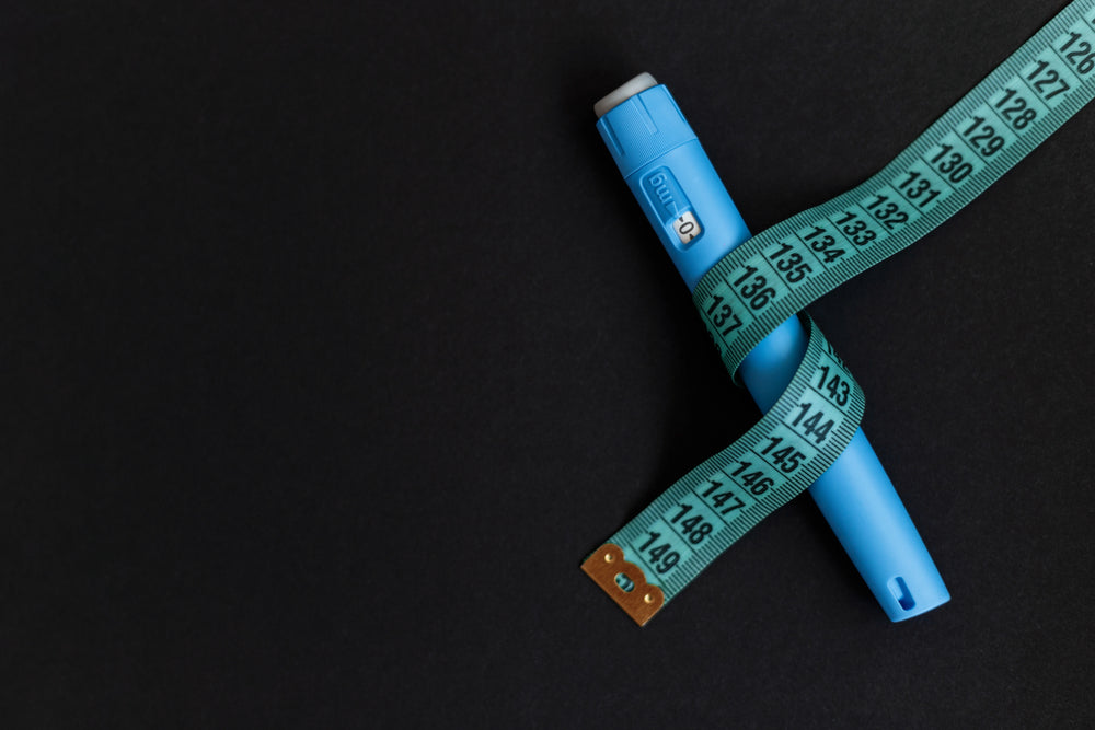 Ozempic injector drug pen with a measuring tape on a black background. Anti diabetes and lower blood sugar levels. Weight loss concept